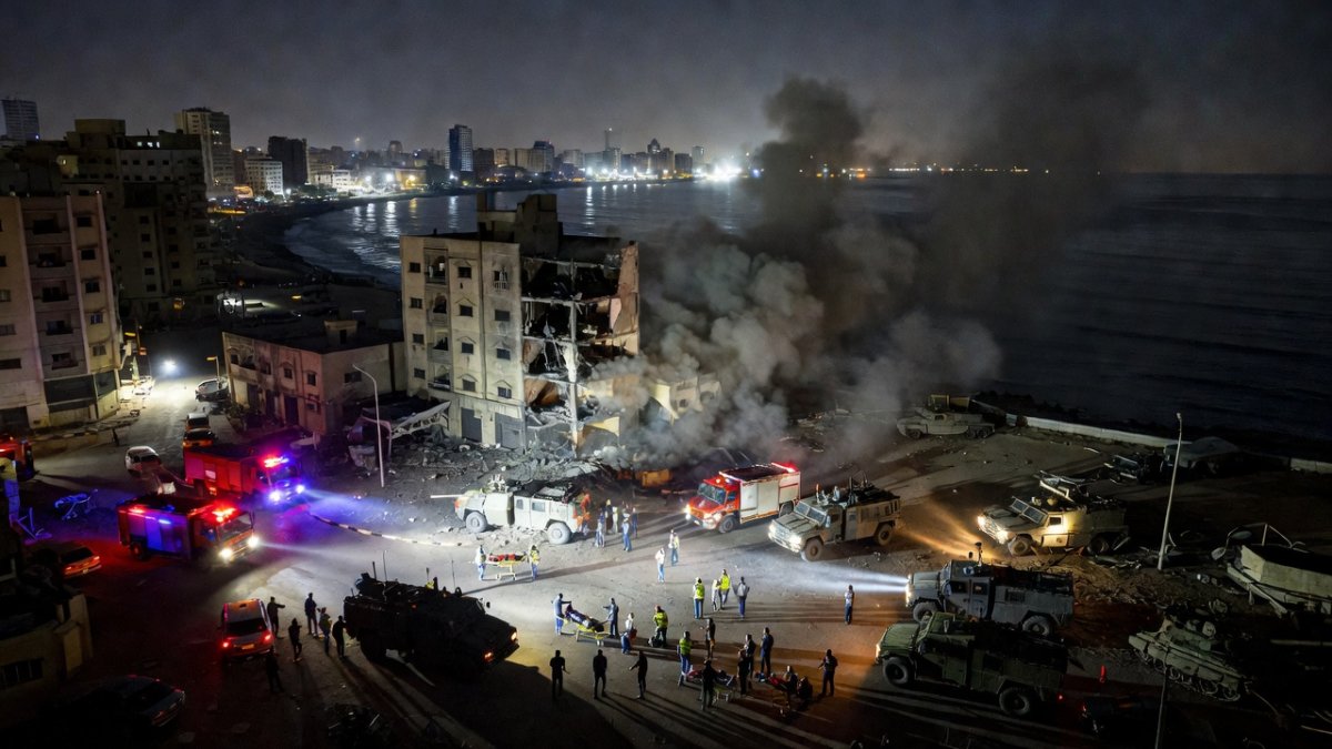 Aerial view of a Middle Eastern city at night showing smoke rising from a strike location near the coastline