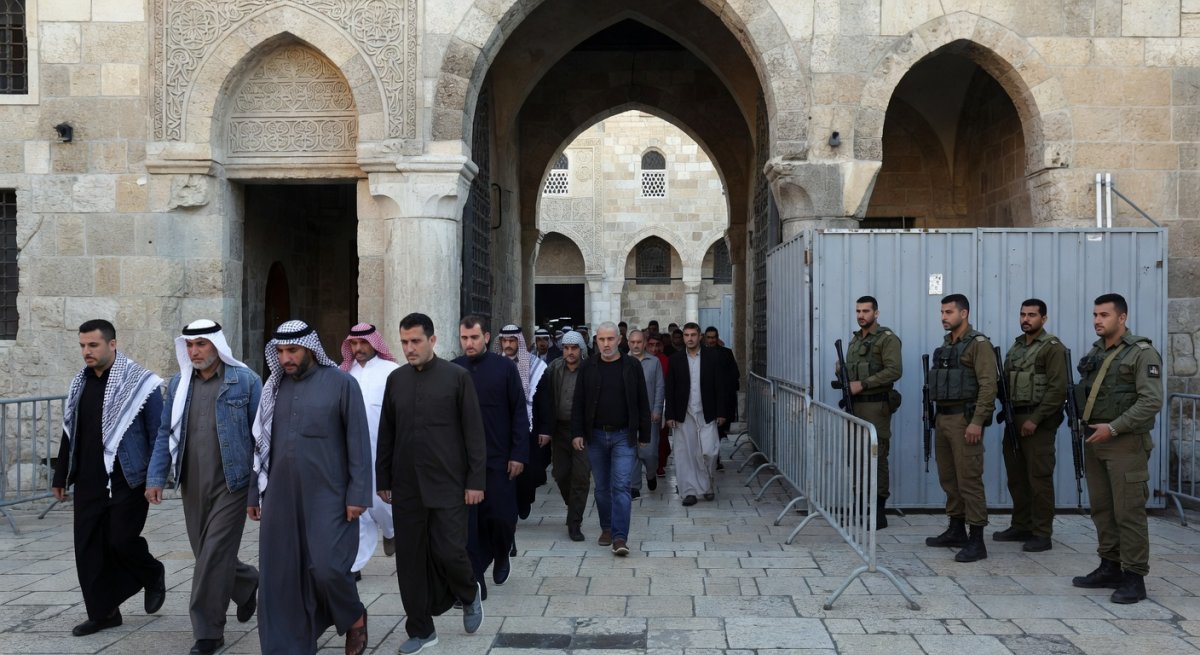 Palestinian worshippers praying at Al-Aqsa with Israeli security presence visible in the background