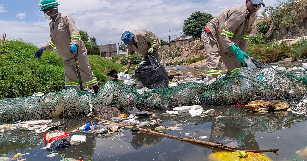 Workers in protective gear collect plastic waste from the polluted Jukskei River in Alexandra, Johannesburg