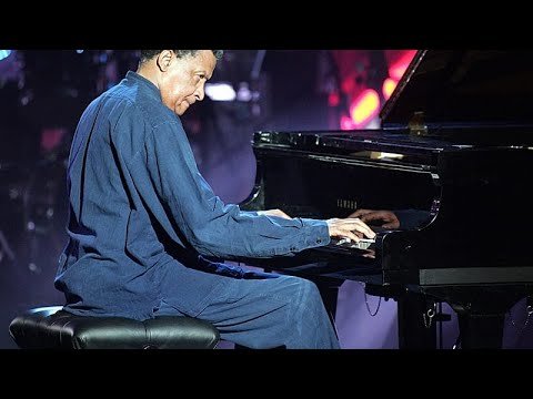 Abdullah Ibrahim in his signature blue outfit playing a grand piano on stage