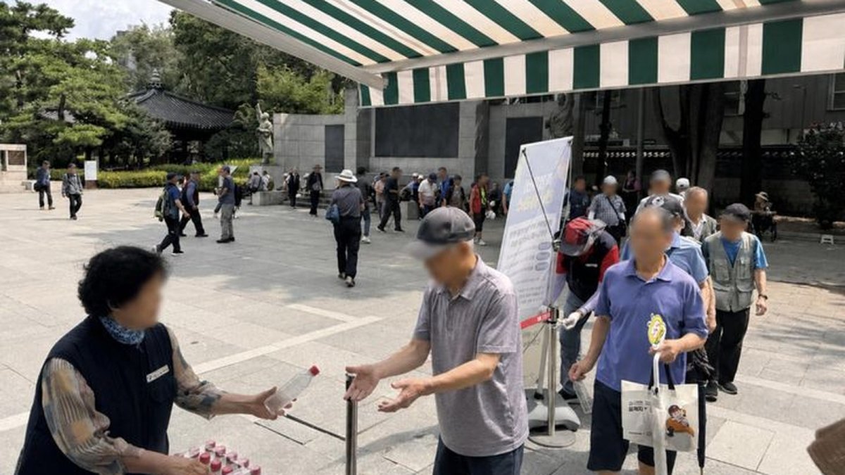Volunteer distributes chilled Arisu bottled water to senior citizens at Tapgol Park in Seoul