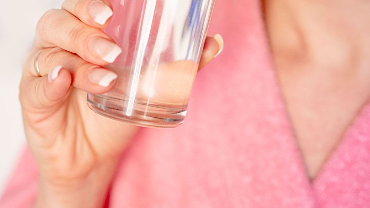A woman drinking a glass of water — hydration needs vary by weight, climate and activity