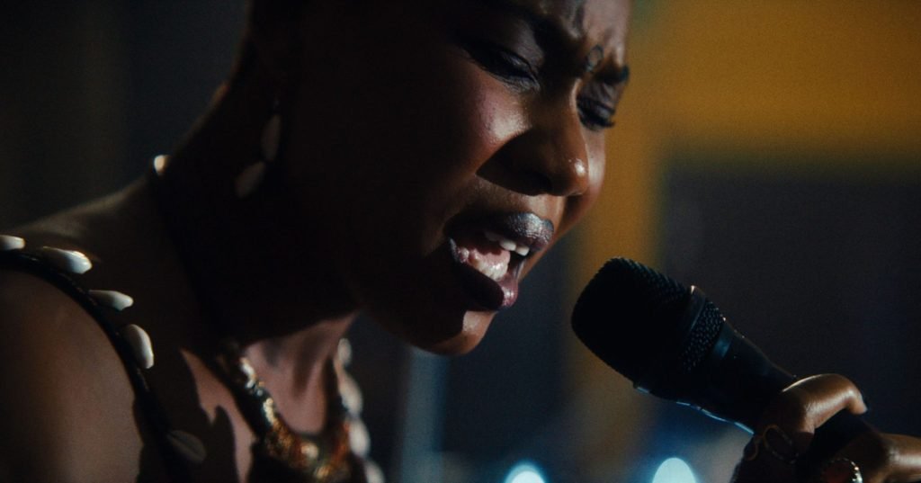 A singer performs with intensity in a dramatic, dimly lit scene from the Nigerian film Dear Ajayi