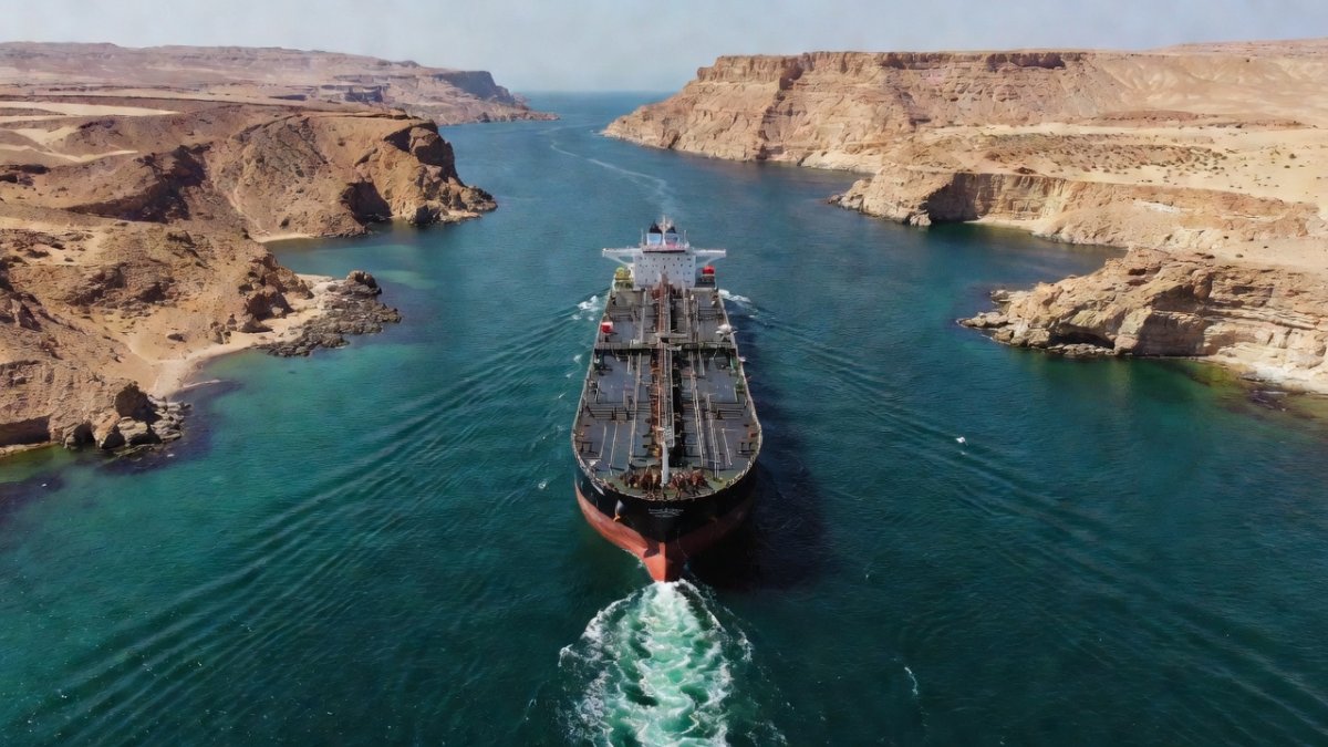 Tanker ships navigating the Strait of Hormuz with military escort vessels nearby
