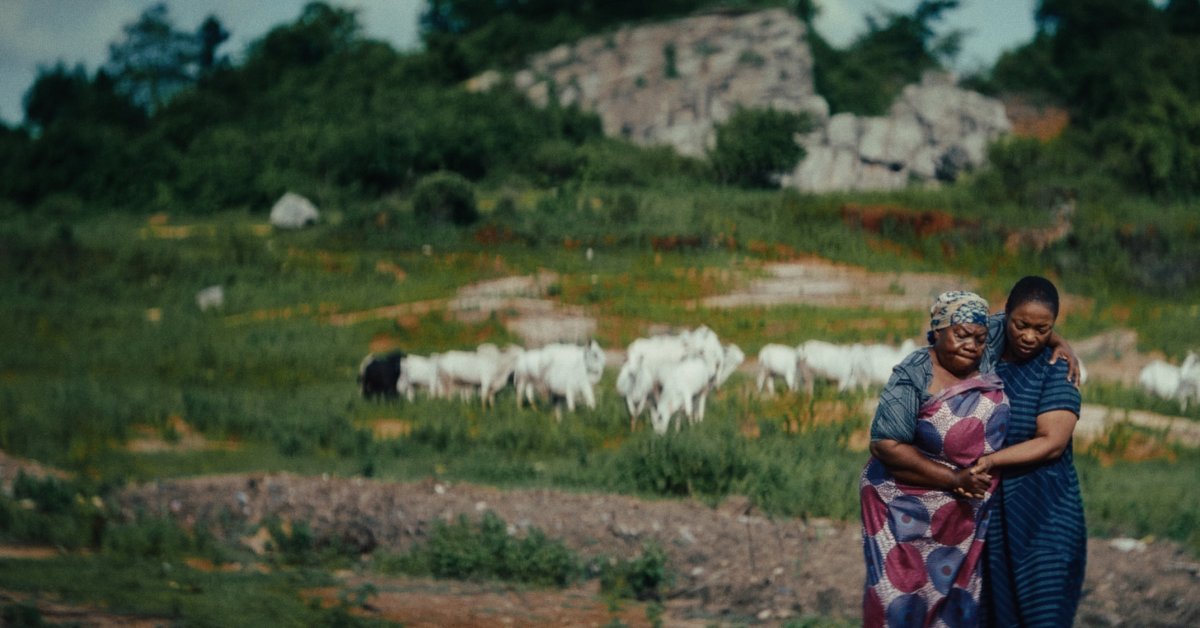 Two women embrace in a rural Nigerian landscape in a scene from Dear Ajayi