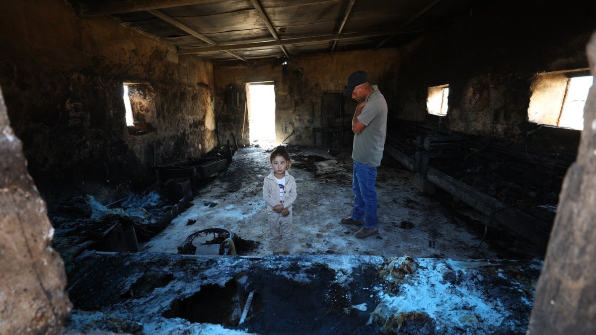 A Palestinian man and girl stand inside a home damaged in a settler attack on Khirbet al-Tuba, Masafer Yatta