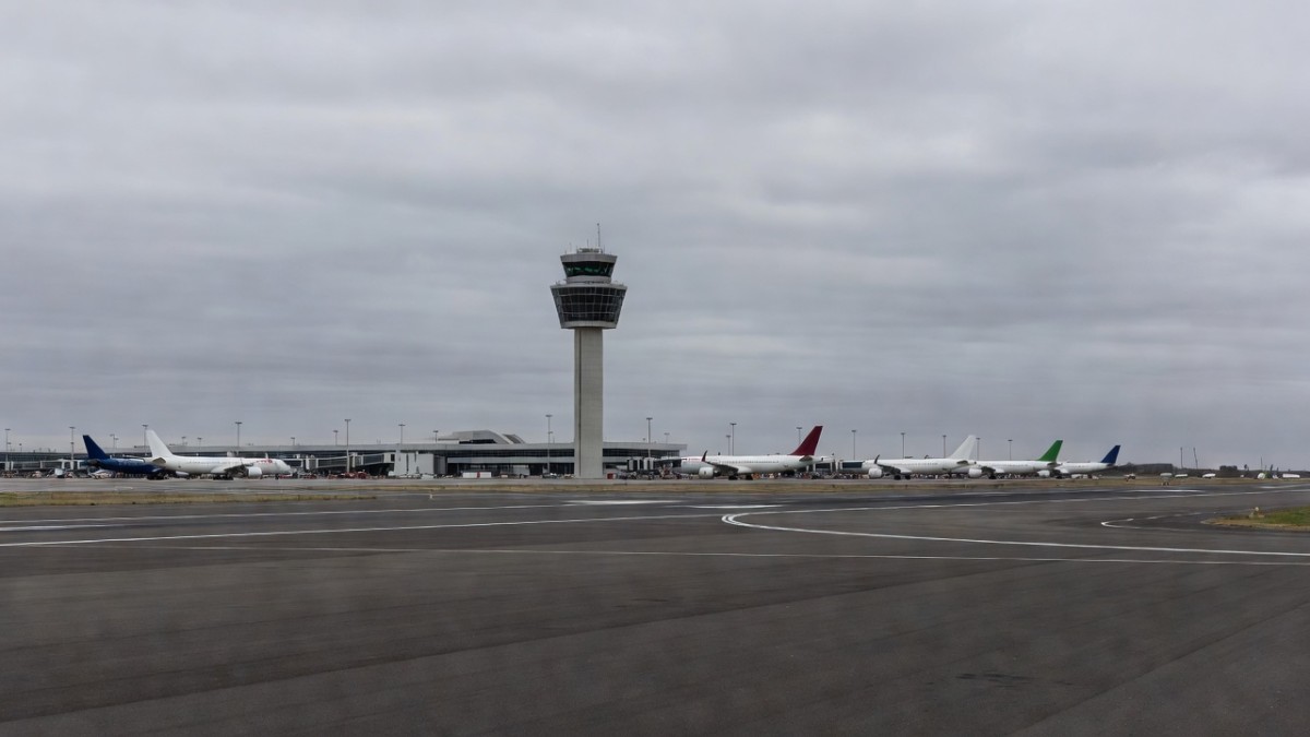 Commercial aircraft parked at terminal gates beside an air traffic control tower at a UK airport