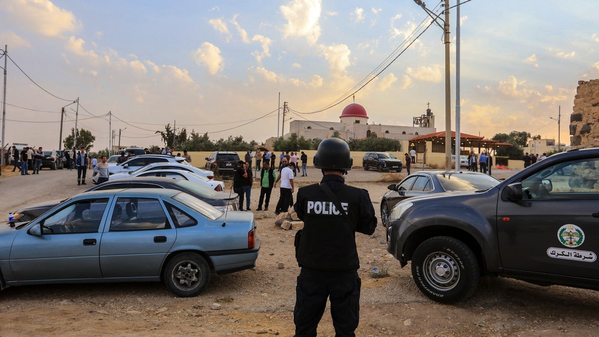 A police officer stands in front of residents near the Greek Orthodox church in Humud village, Karak governorate, Jordan, after a shooting at a funeral on 23 October 2026. Photo: AFP