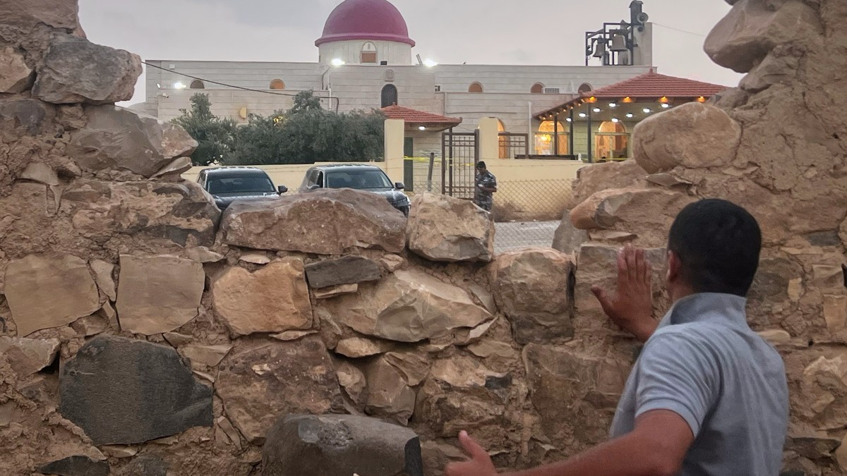 A man looks through a gap in a stone wall toward Saint George's Greek Orthodox Church in Hamoud village, Karak governorate, Jordan, where gunmen opened fire during a funeral on 23 October 2026. Photo: Associated Press