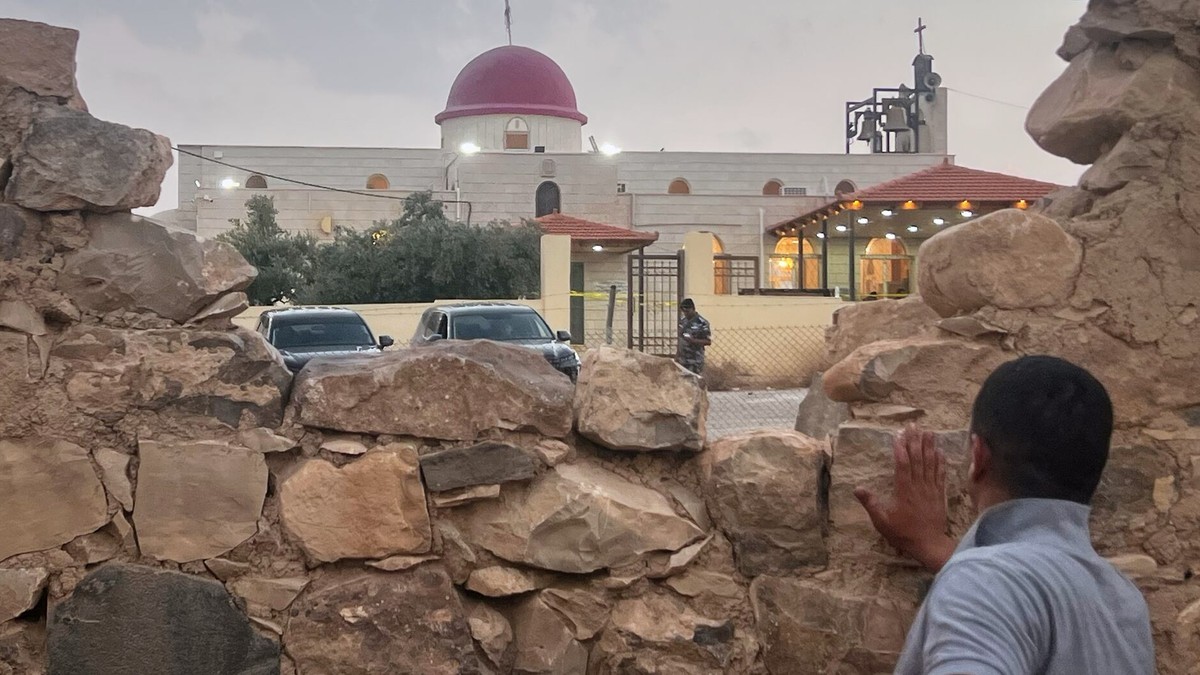 A man looks through a gap in a stone wall toward a Greek Orthodox church in Humud village, Karak governorate, Jordan, where gunmen opened fire during a funeral on 23 October 2026. Photo: AP