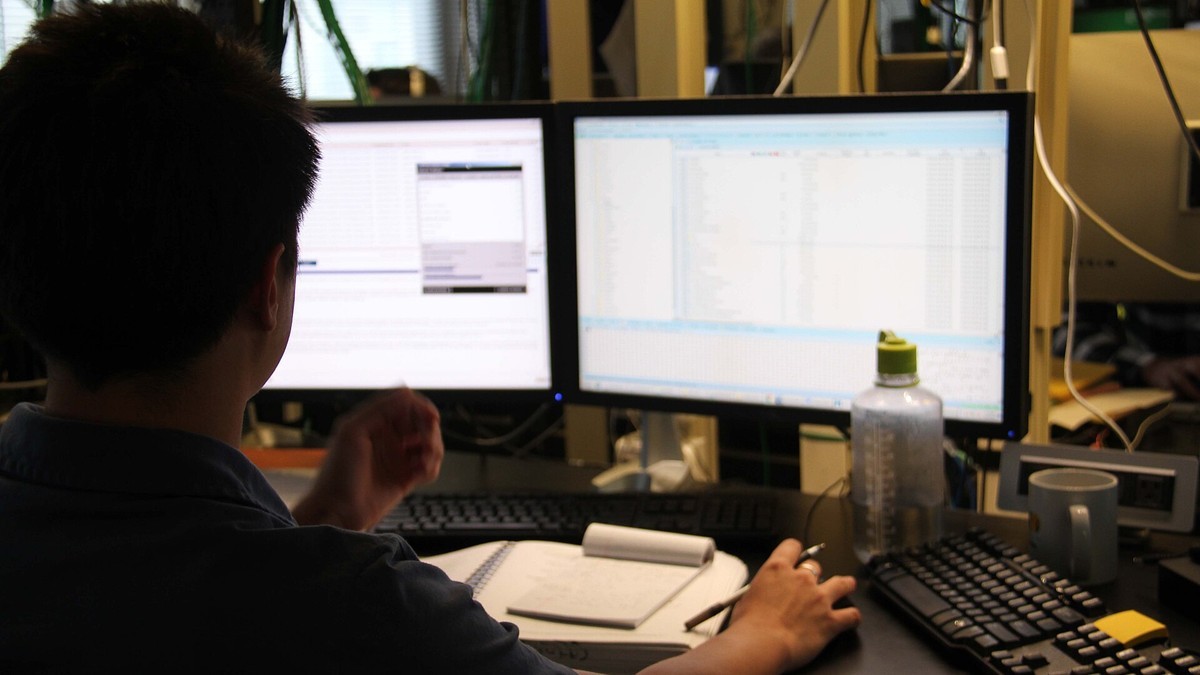 A security analyst reviews data on two monitors at a workstation, with server racks behind. Photo: U.S. Diplomatic Security Service, public domain
