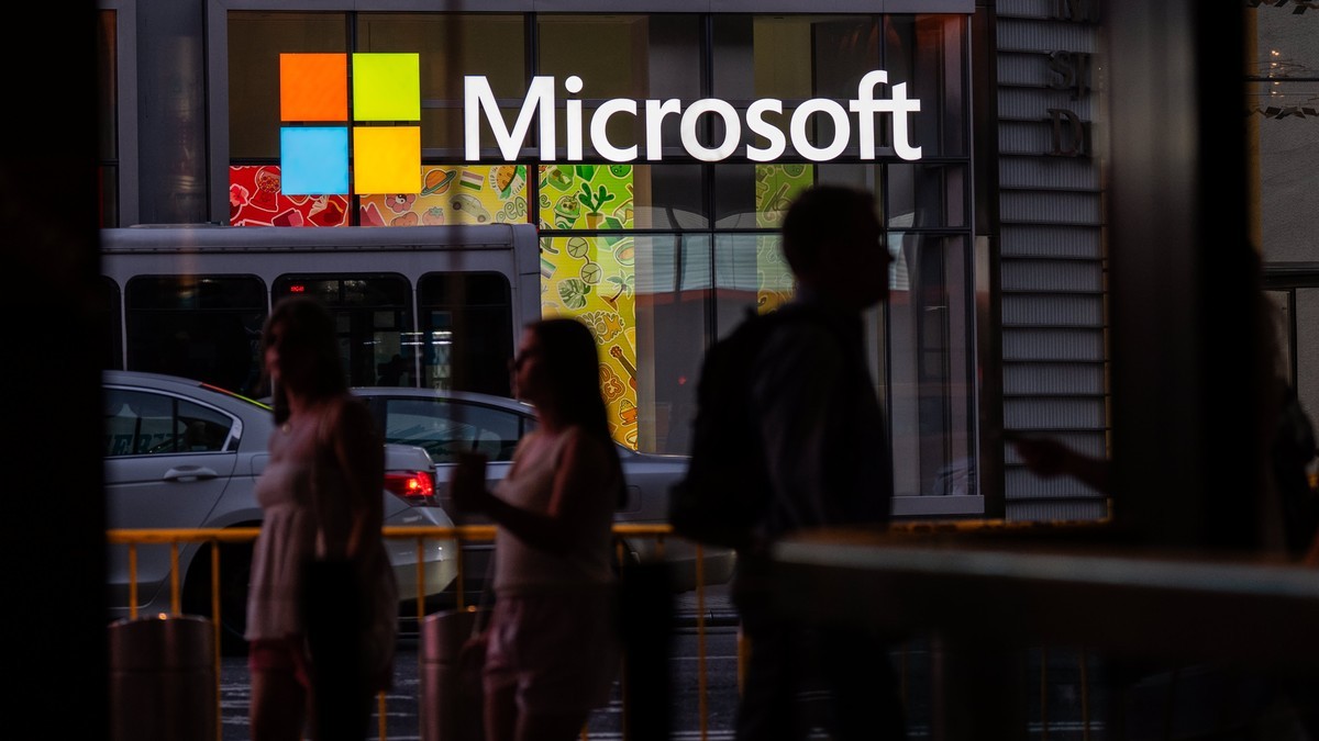 Pedestrians pass a brightly lit Microsoft sign on a city street at night. Photo: CNBC