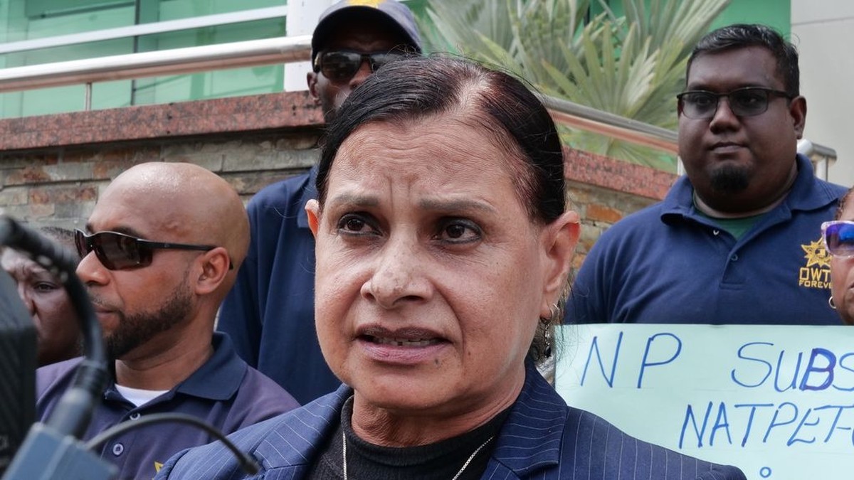 A trade union official speaks into a microphone beside workers at a media conference in Trinidad. Photo: Guardian Media